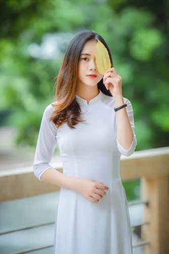 Một bức hình e ấp và thu hút với cách tạo dáng đứng thẳng và một cây cầm lá che nửa mặt