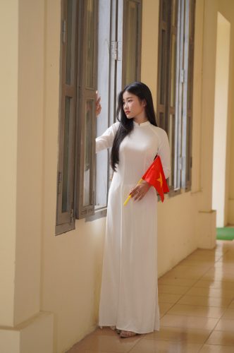 Ảnh cận bạn nữ mặc áo dài tạo dáng tại hành lang mái vòm, với ánh nắng chiếu xiên qua các trụ cột.